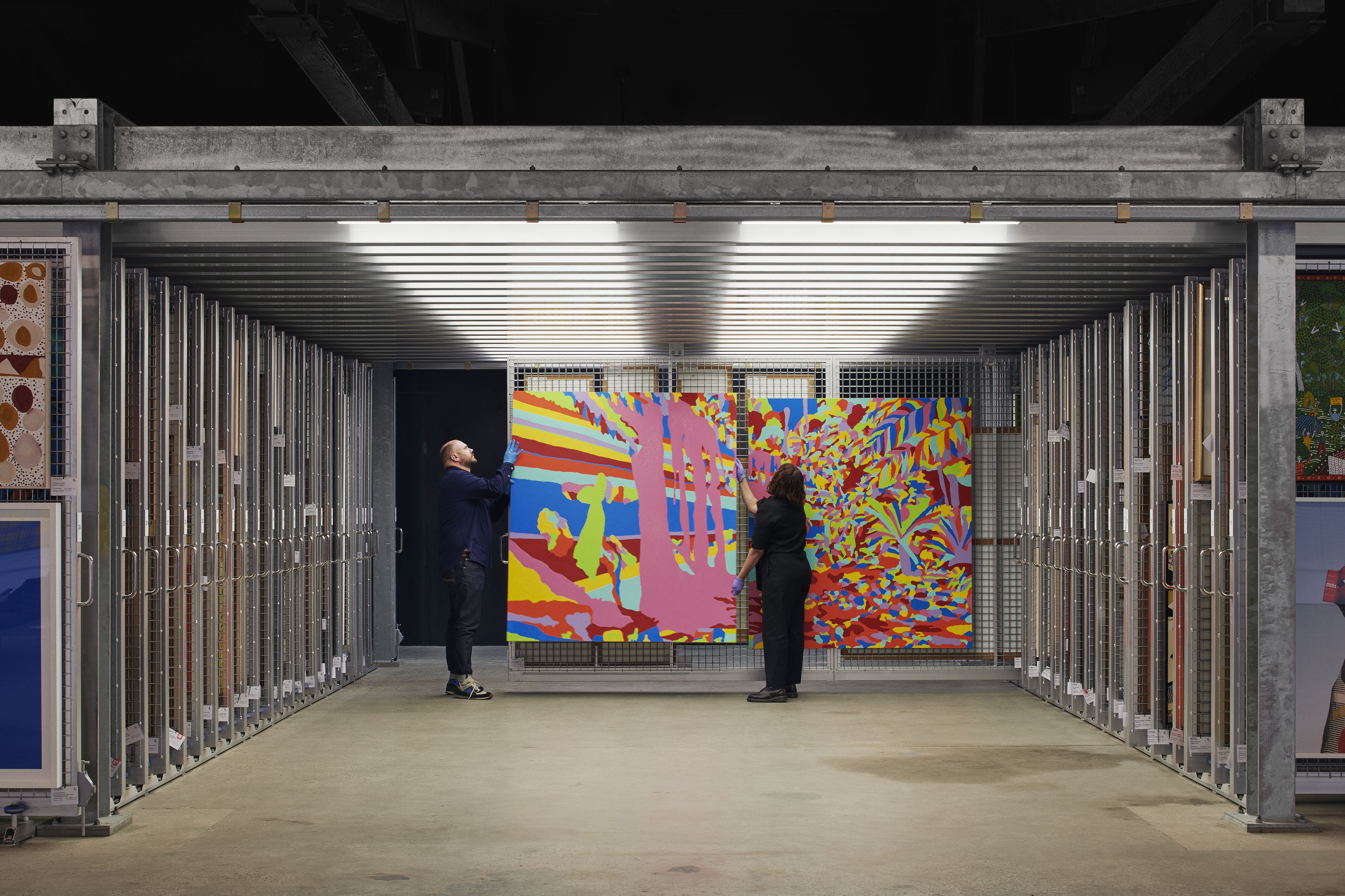 Artbank Curator Paul Adair and Collections Officer Katie Tremschnig in the Artbank Melbourne collection store, 2025.  Artwork featured is Jemima Wyman, Scapeology (Waterfall), 2005. Photo by Nicole England