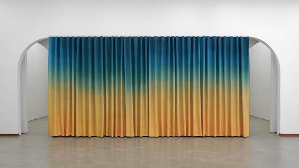 Photo of a vibrantly coloured curtain hanging across arched doorways. The curtain is blue blending into yellow, and the interior walls are white with polished concrete floors. Photo by Ryan Renshaw. Courtesy of the Artist and The Renshaws', Brisbane
